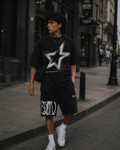 Person wearing a black graphic t-shirt and shorts on a city street.