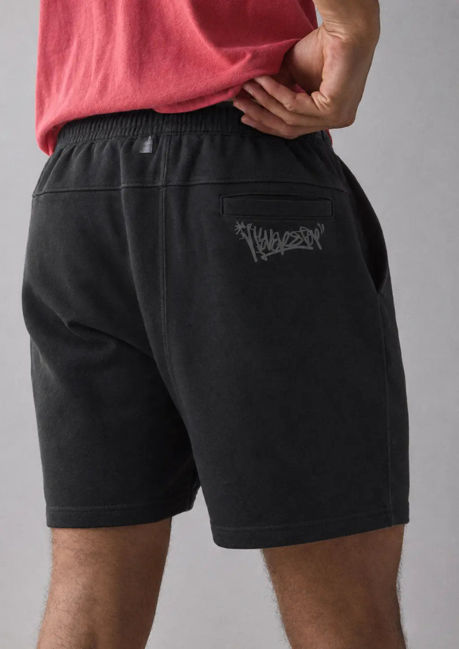 Person wearing black shorts with a logo on a gray background