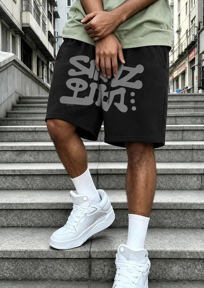 Person wearing black shorts with white text and white sneakers on a staircase.