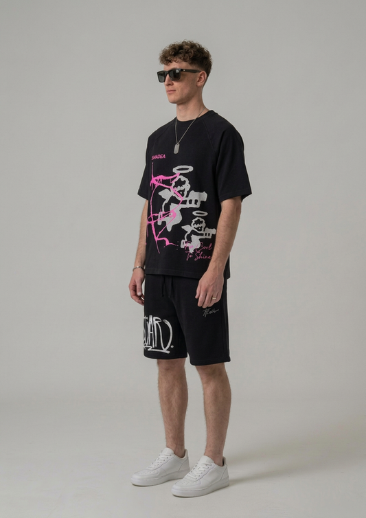 Man wearing a black graphic t-shirt and shorts with sunglasses on a plain background